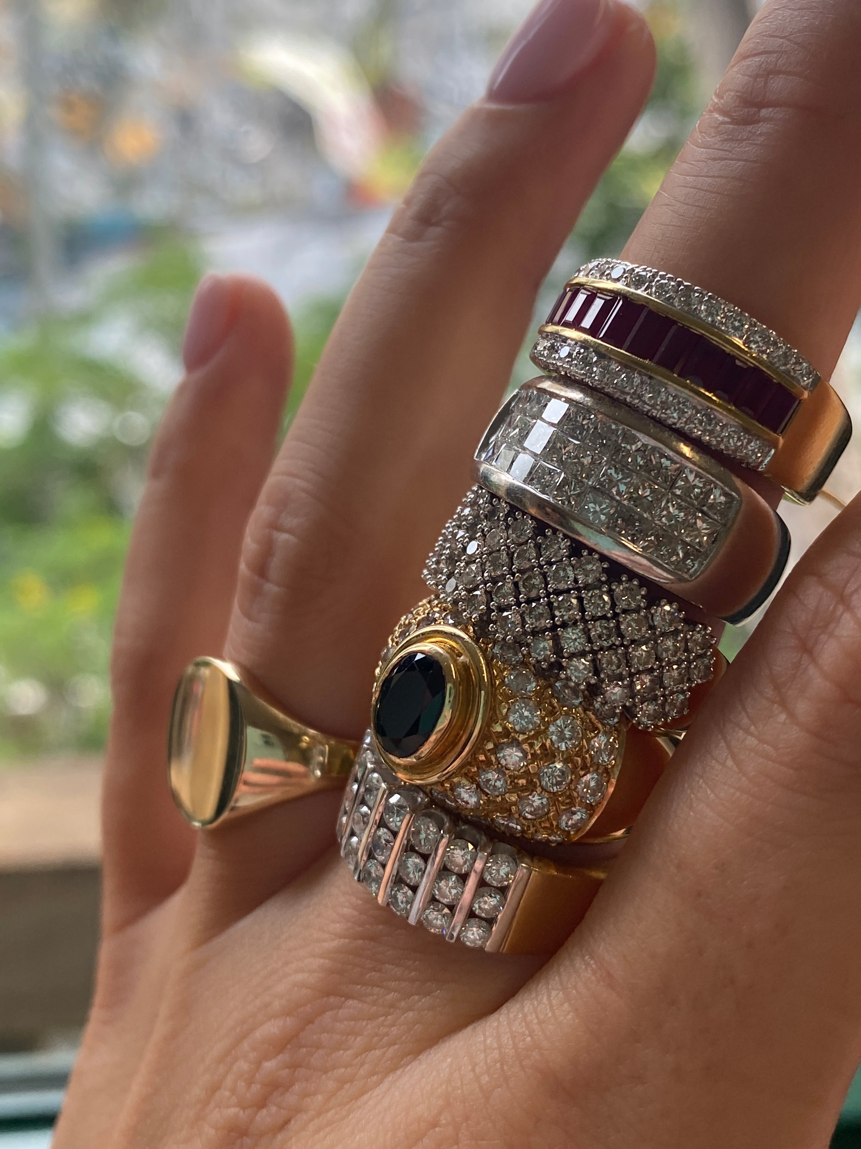 Hand wearing multiple ornate rings with gemstones and gold accents.