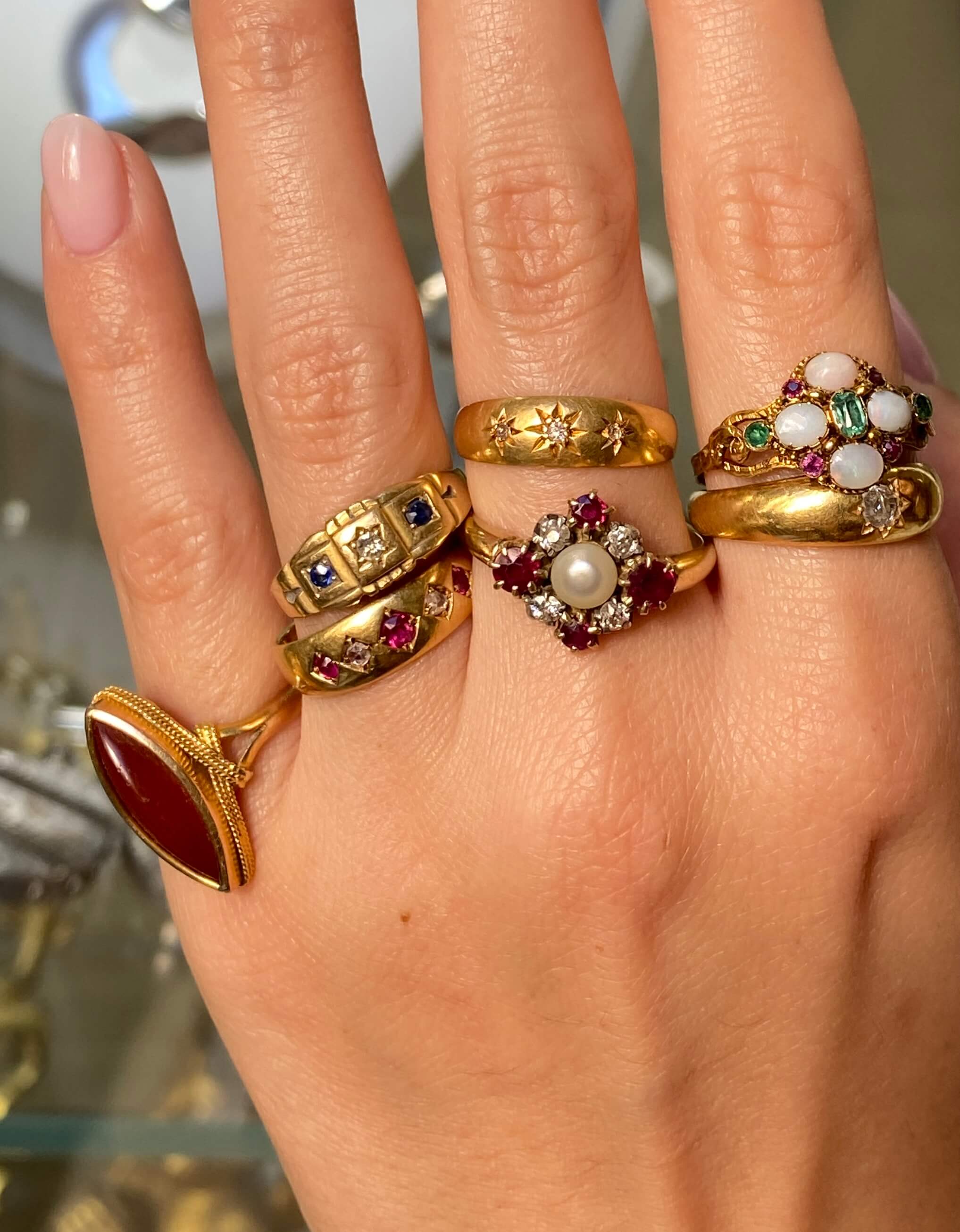 A close-up of a hand wearing multiple vintage gold rings with various gemstone and pearl details.