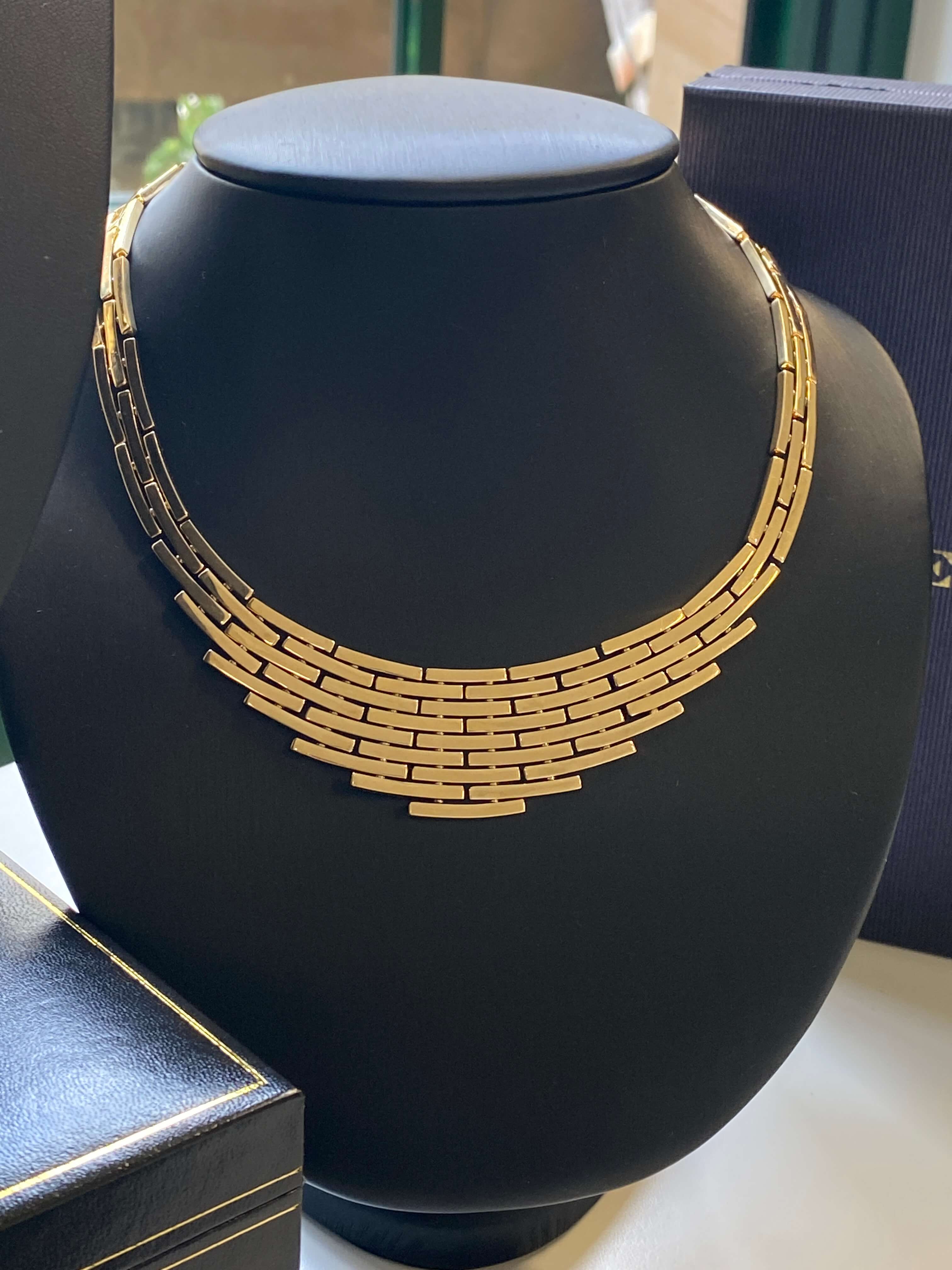 A gold multi-strand chain necklace displayed on a black jewelry bust, with dark presentation boxes partially visible in the background.
