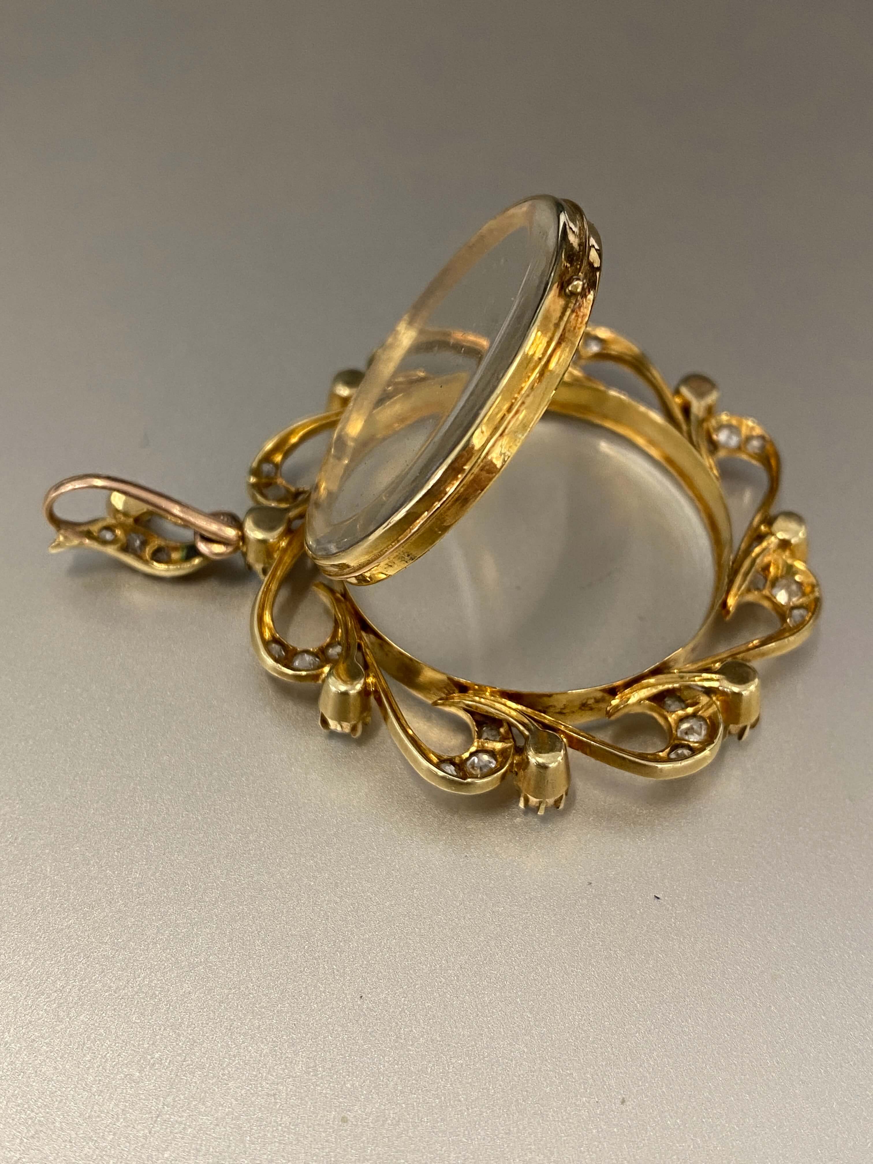 antique gold photo locket with hinged clear glass cover, photographed on a neutral gray background.