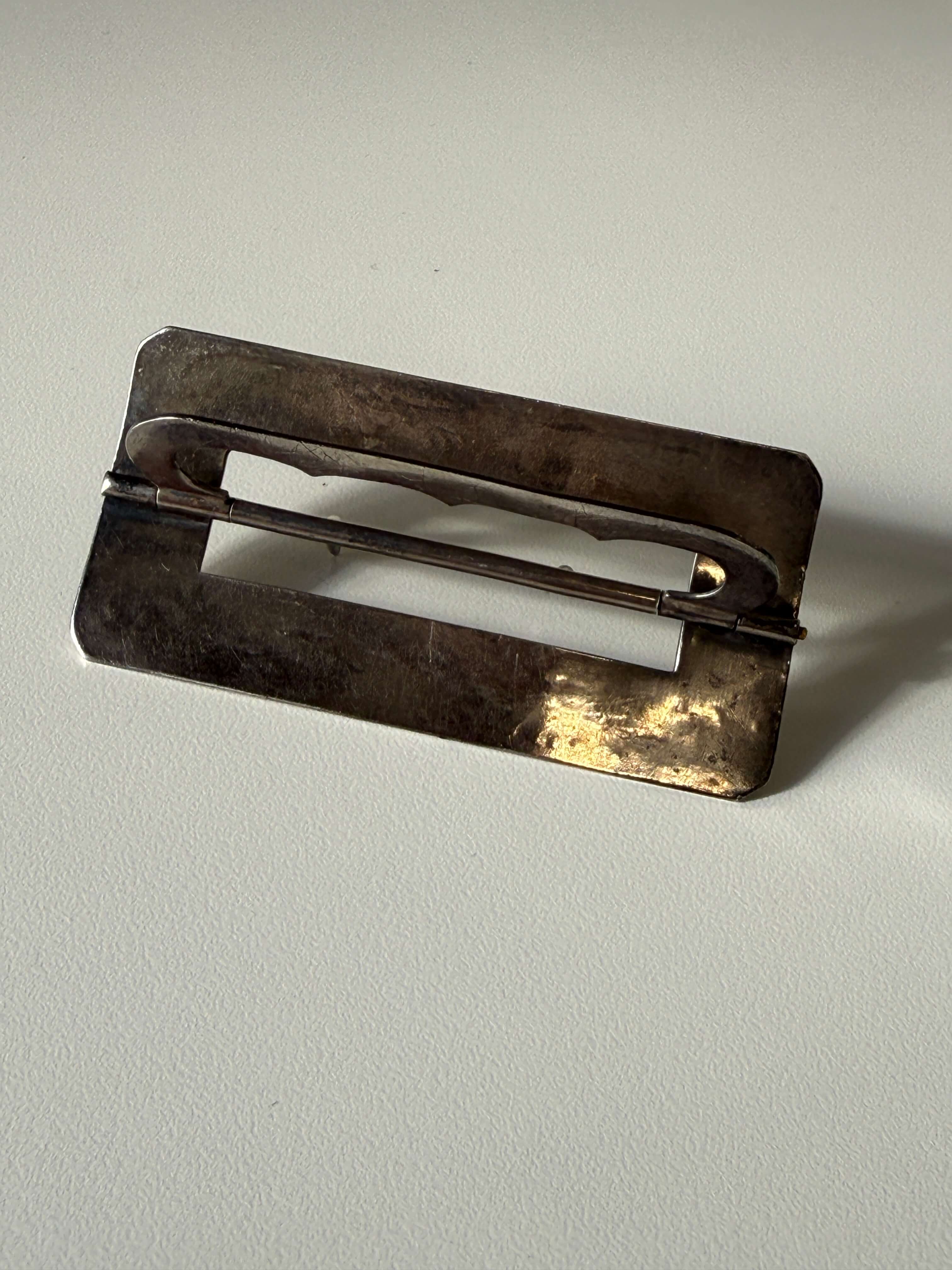 The reverse of a silver-toned metal belt buckle shown against a plain white background.