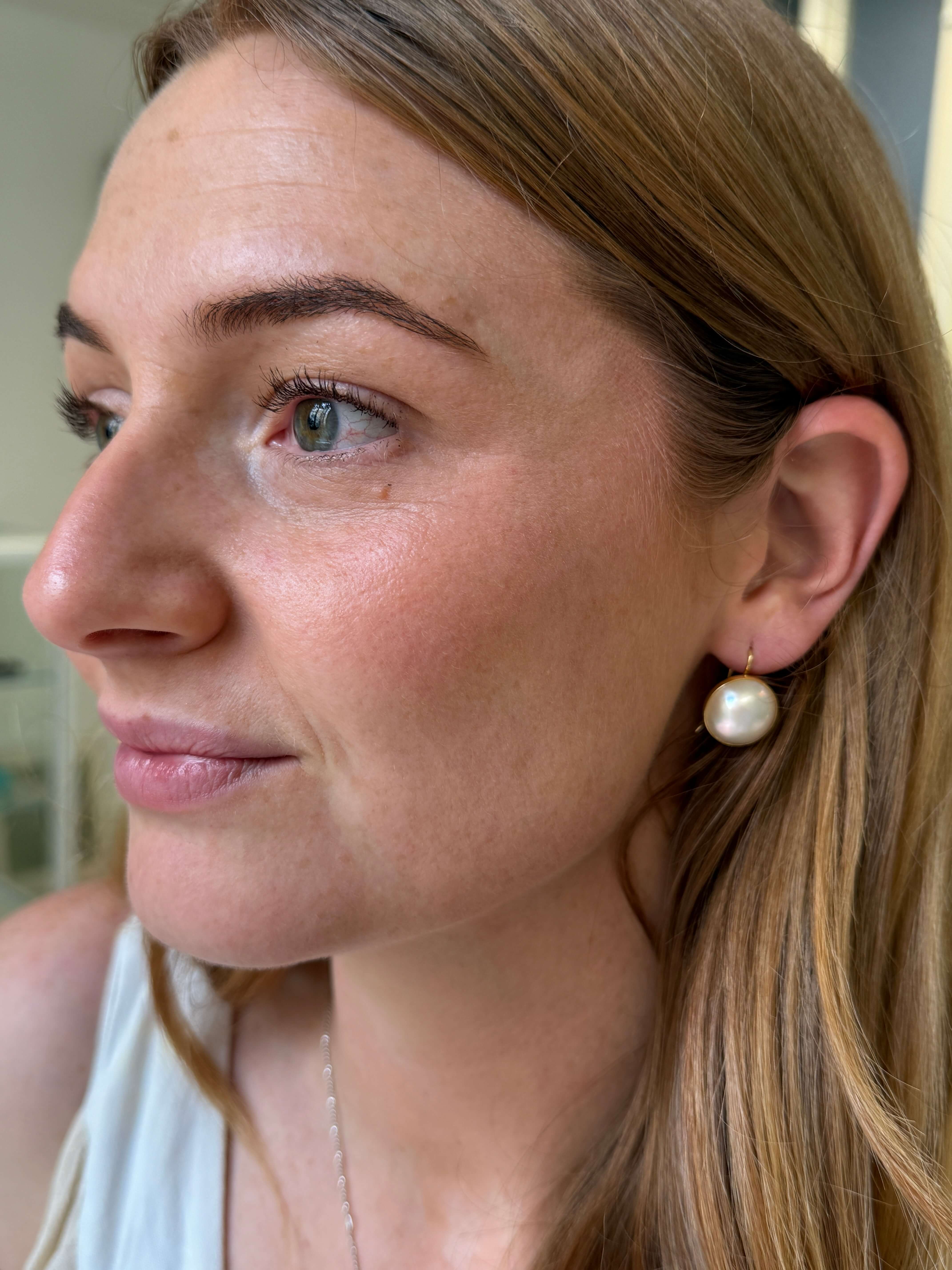 A close-up side profile of a woman wearing yellow gold mabe pearl drop earrings