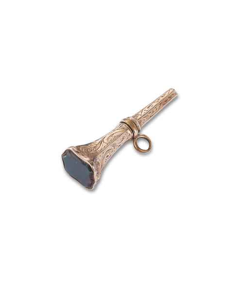 An antique gold watch key with engraved detailing and a dark faceted stone on the front, shown on a plain white background.