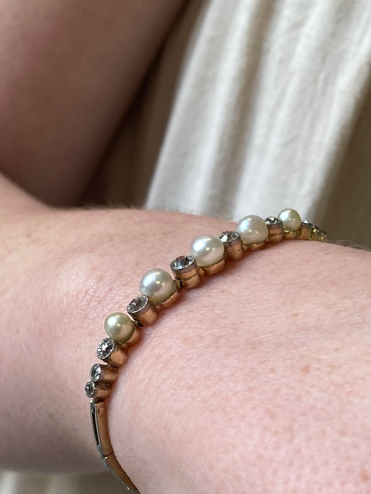 A close-up of a gold bangle bracelet with white pearls and old cut diamonds worn on a person's wrist.