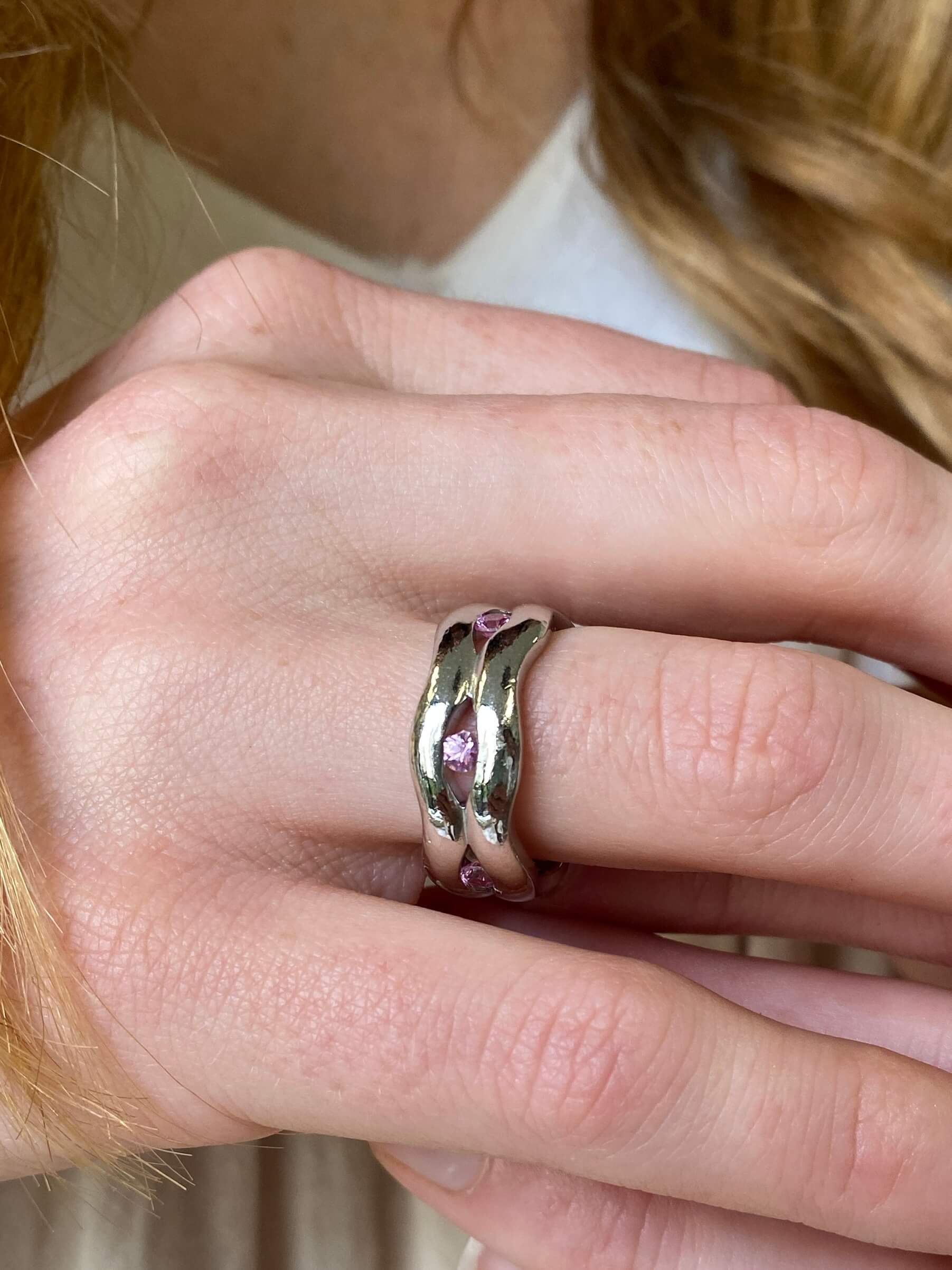 A close-up of a person's hand wearing a polished platinum ring with small pink sapphire accents.