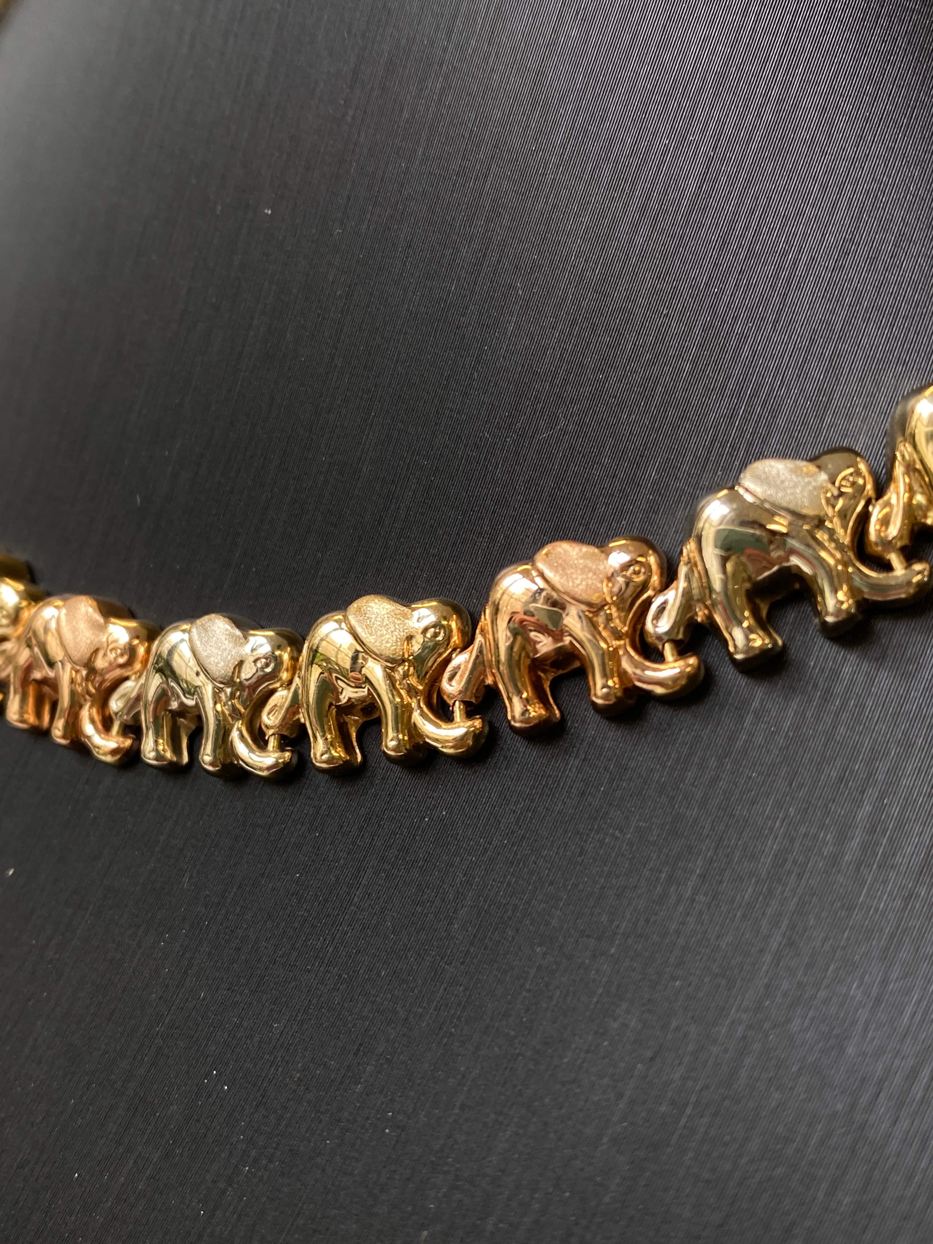 A close-up of a gold-toned chain bracelet featuring a repeating pattern of small elephant charms, displayed on a dark textured surface.