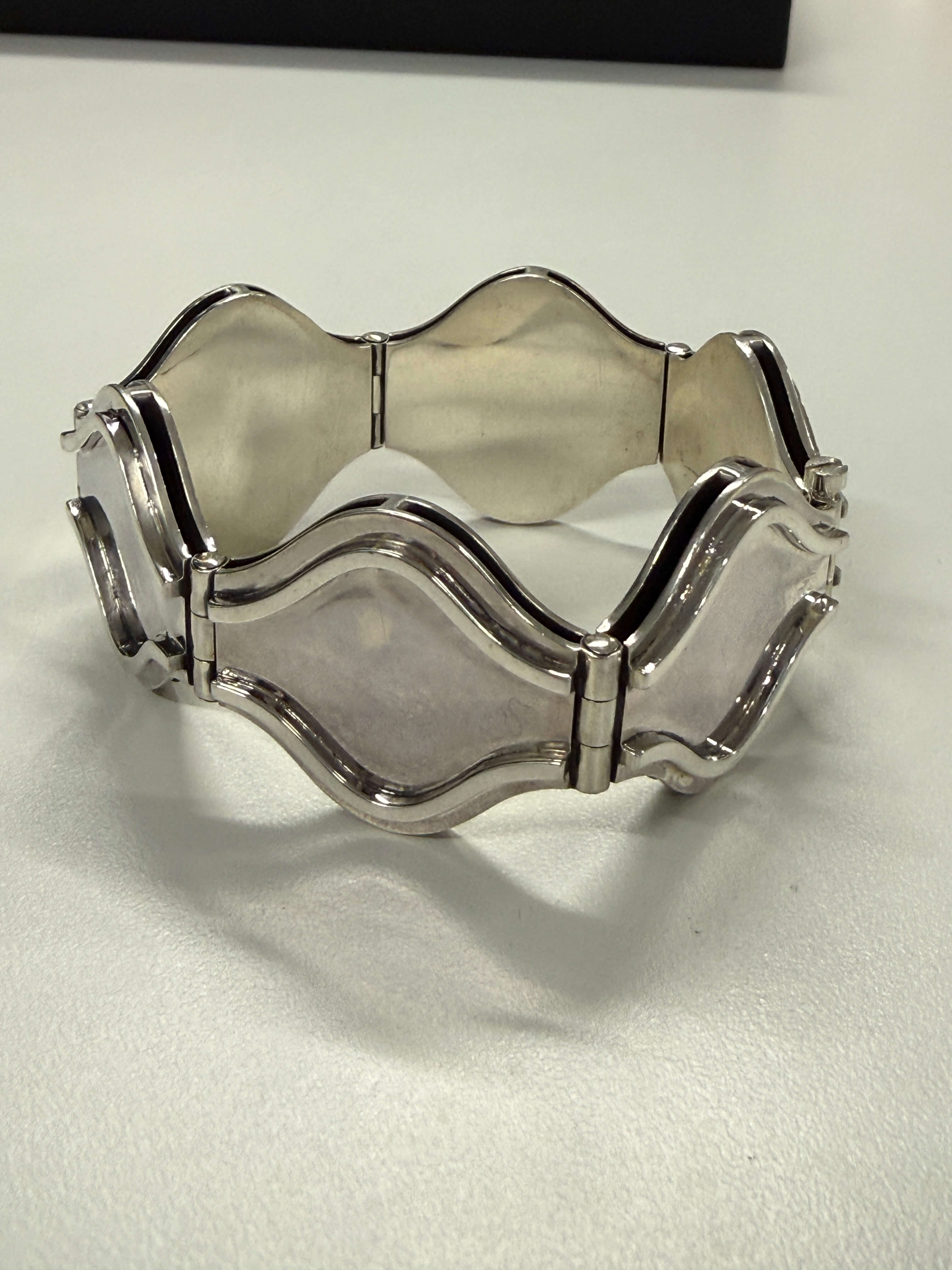 A wide silver cuff bracelet with wavy, scalloped edges and smooth, polished inlay panels, displayed on a light gray surface.